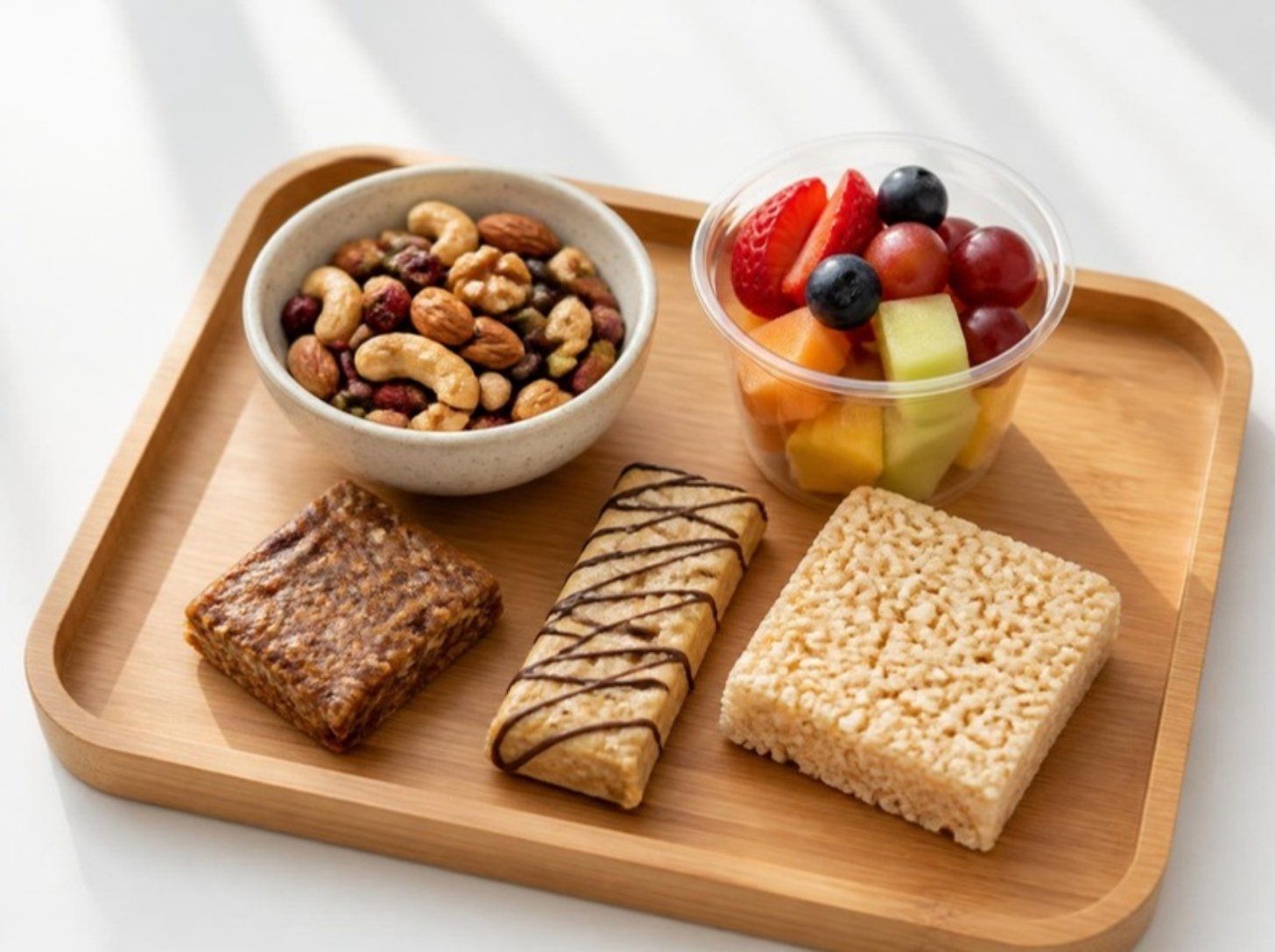 Mixed nuts, a fruit cup, protein bars and a rice crispy treat on a bamboo tray